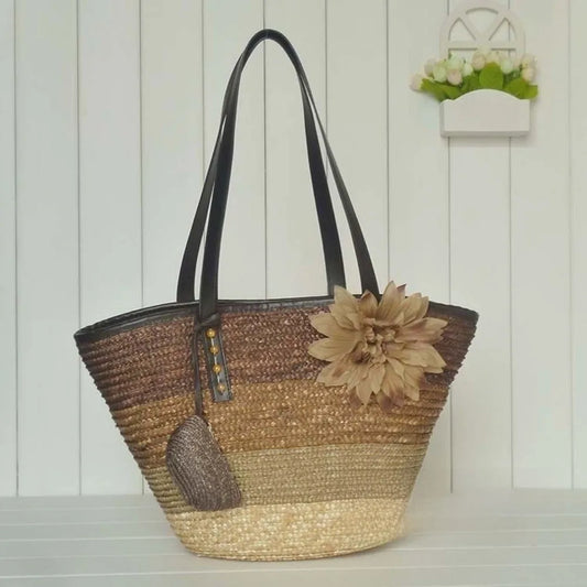 Woven handbag with a large flower accessory on a wooden surface.