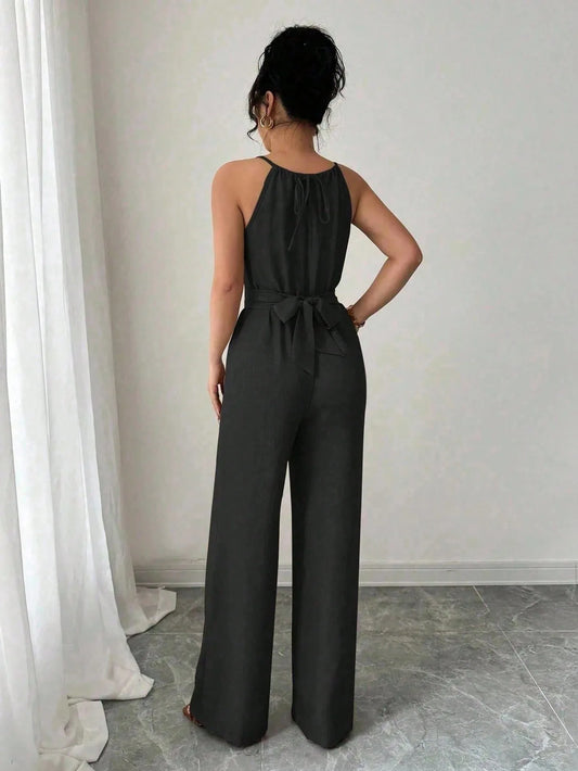 Woman wearing a black jumpsuit standing in a room with white curtains and gray floor.