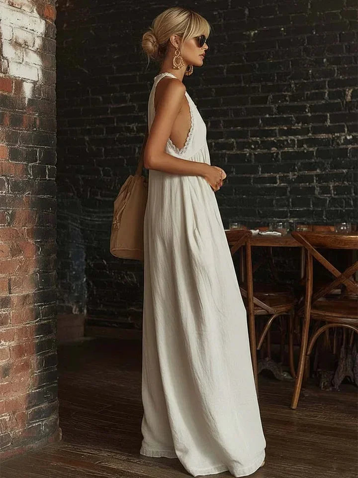 Woman in a white dress standing against a brick wall in an indoor setting.