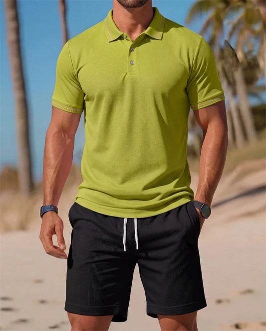 Man wearing a green polo shirt and black shorts on a beach.