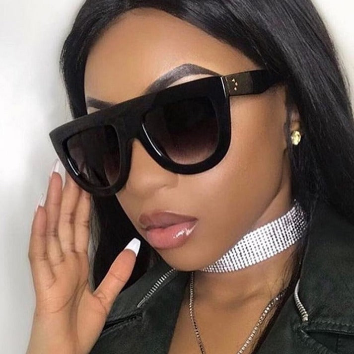 Woman wearing black sunglasses and a black jacket with a white background