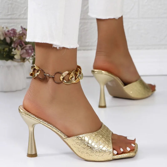 Gold high-heeled shoes with chain anklet on a white background