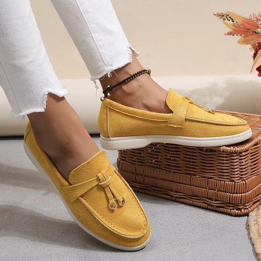 Yellow loafers worn with white jeans on a neutral background