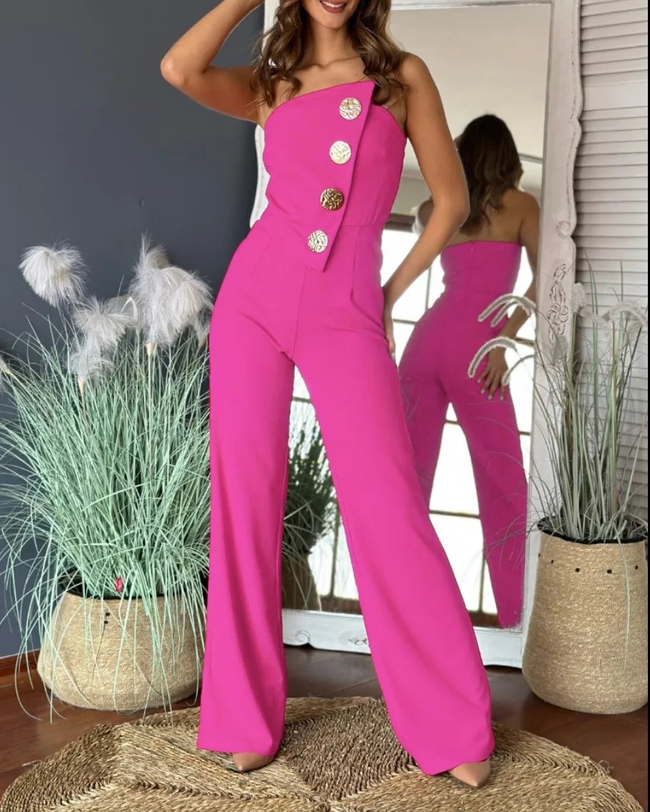 Woman wearing a bright pink jumpsuit with buttons in a room with plants and a mirror.