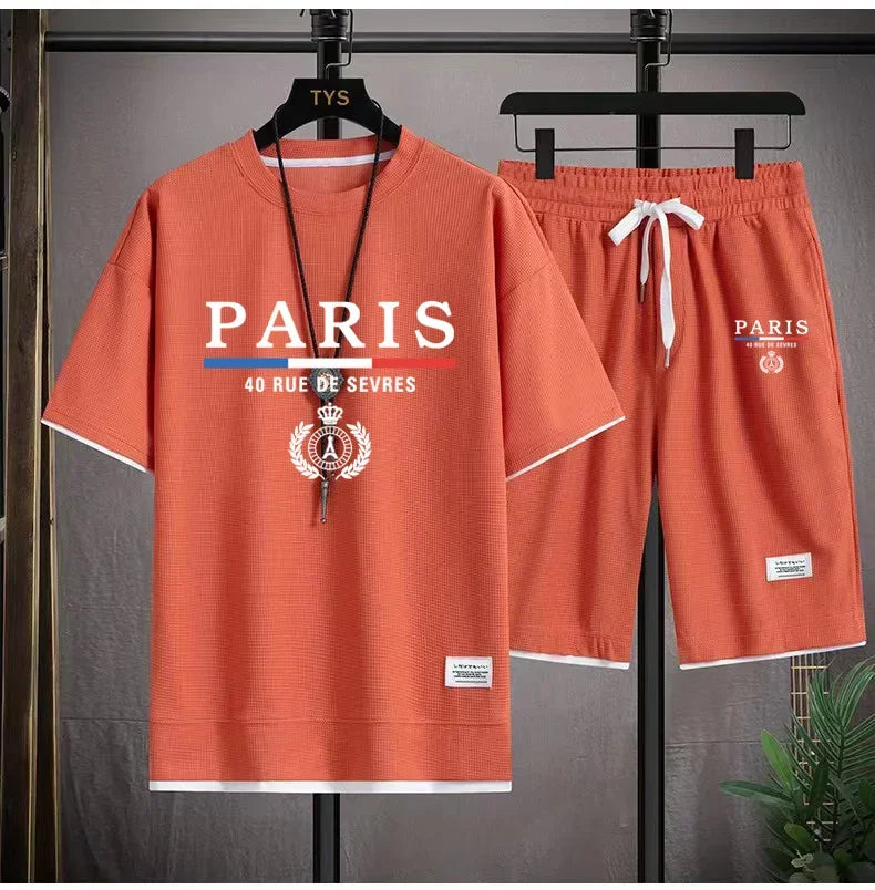 Orange t-shirt and shorts set with 'PARIS' branding on hangers against a gray background.