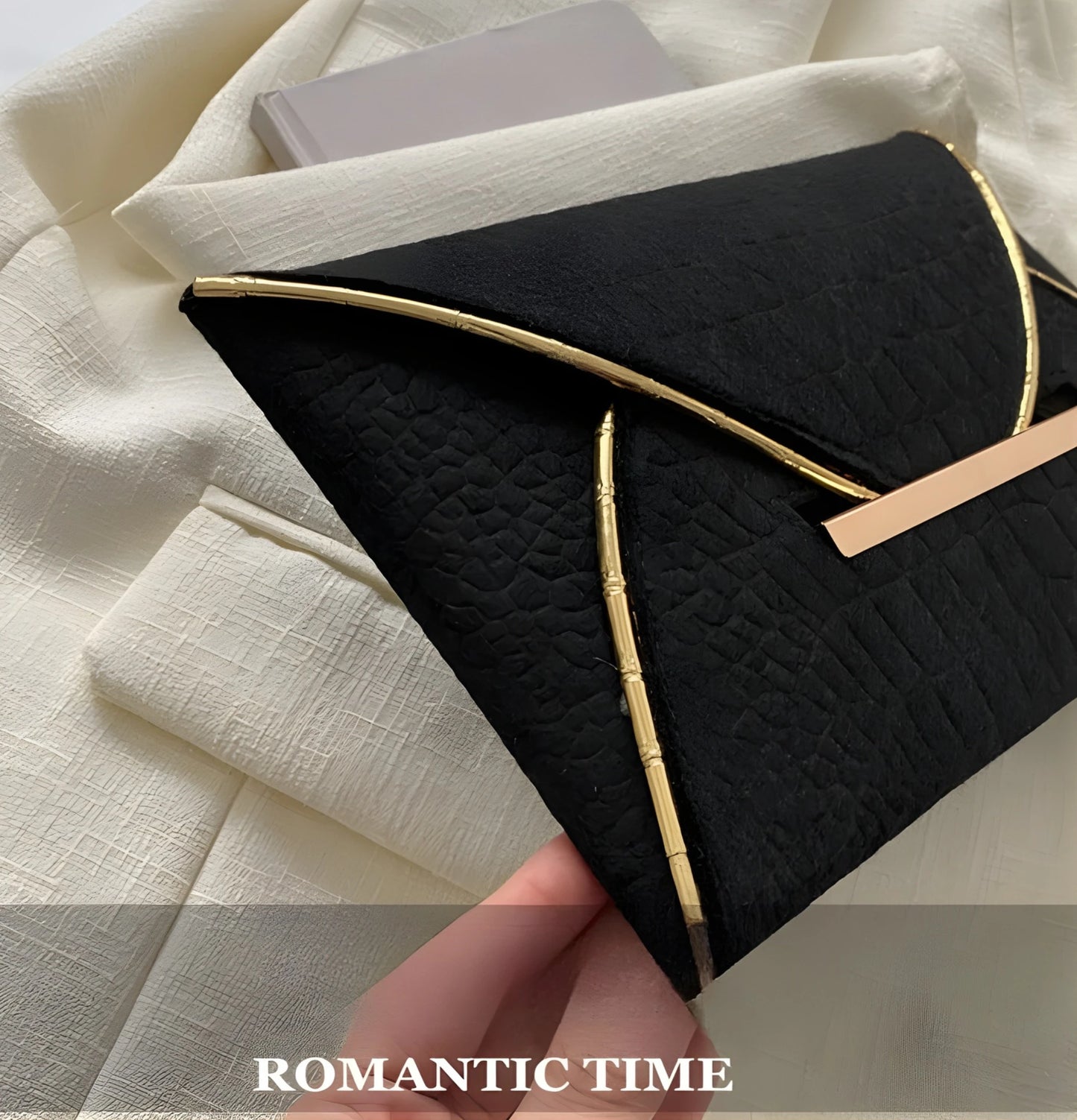 Black textured clutch bag with gold trim on a white fabric background