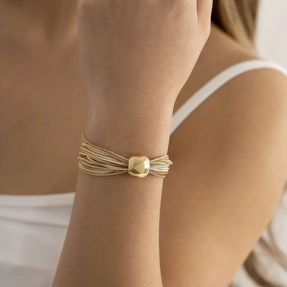 Gold-tone multi-strand chain bracelet with a smooth rounded centerpiece, shown on a woman's wrist with a white sleeveless top.