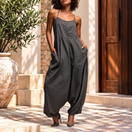 Woman wearing the Elegant Spaghetti Strap Wide Leg Jumpsuit in charcoal gray, featuring thin shoulder straps, a relaxed fit, spacious side pockets, and flowing wide-leg pants with cuffed hems, styled with gray pointed heels against an elegant Mediterranean resort backdrop.