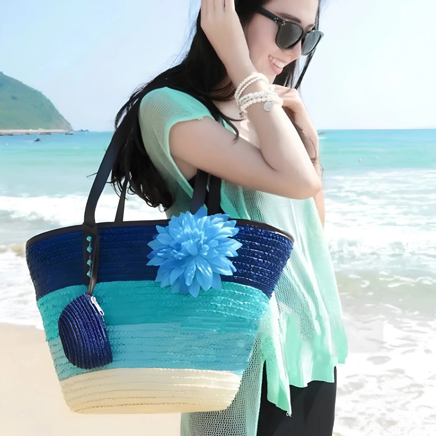 Woman on a beach holding a colorful straw bag with a blue flower.