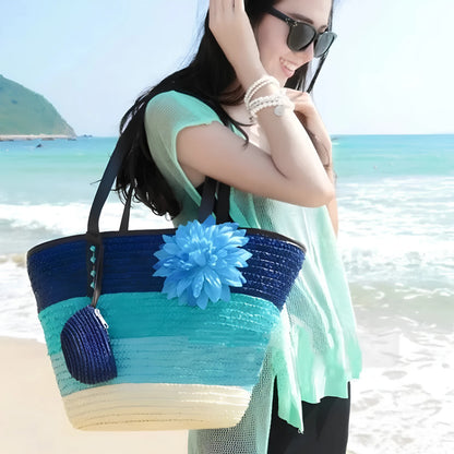 Woman on a beach holding a colorful straw bag with a blue flower.