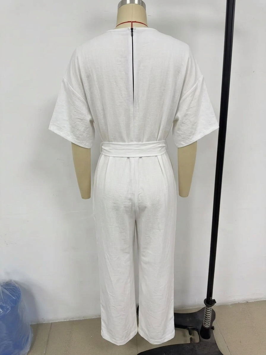 White short-sleeve jumpsuit with a matching waist belt, displayed on a mannequin from the back. The jumpsuit features a relaxed fit and wide legs, with a visible center back zipper.