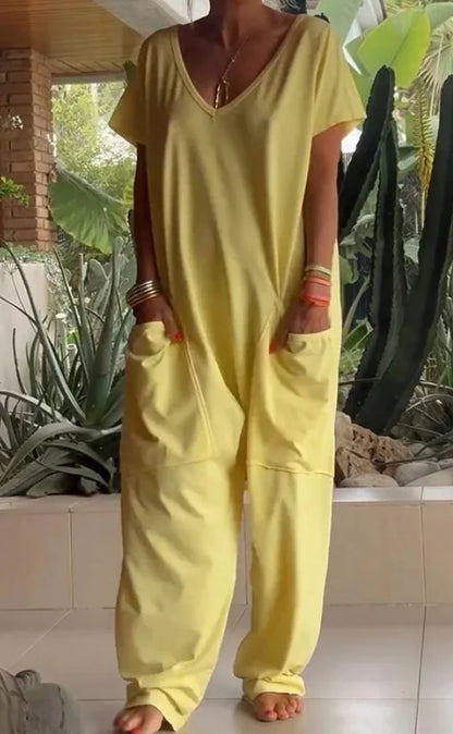 Person wearing a yellow jumpsuit standing in a garden with plants and a brick wall in the background.