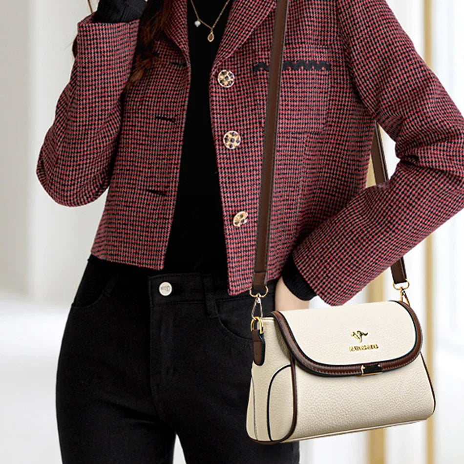 A woman wearing a red and black micro-check blazer over a black top and black pants, carrying a cream-colored shoulder bag with brown trim and gold hardware.