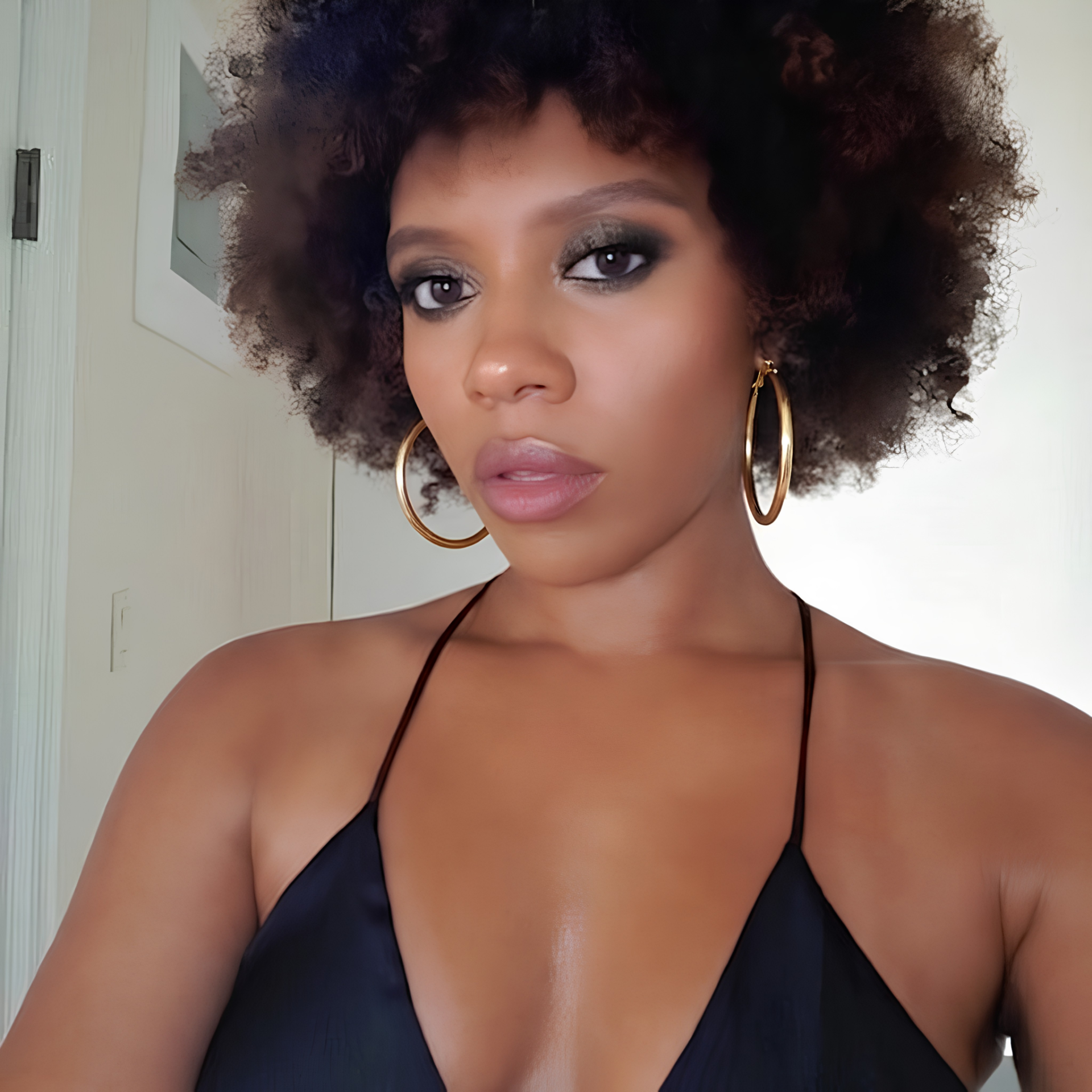 Woman wearing a black strappy top indoors in gold hoop earring