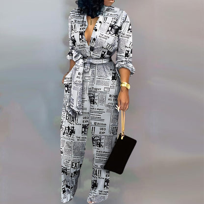 Full-body shot of a trendy outfit: a black-and-white jumpsuit patterned like vintage newspaper pages, styled with rolled-up sleeves and a cinched waist. Accessories include a black rectangular bag, shiny silver heels, and a gold wristwatch.