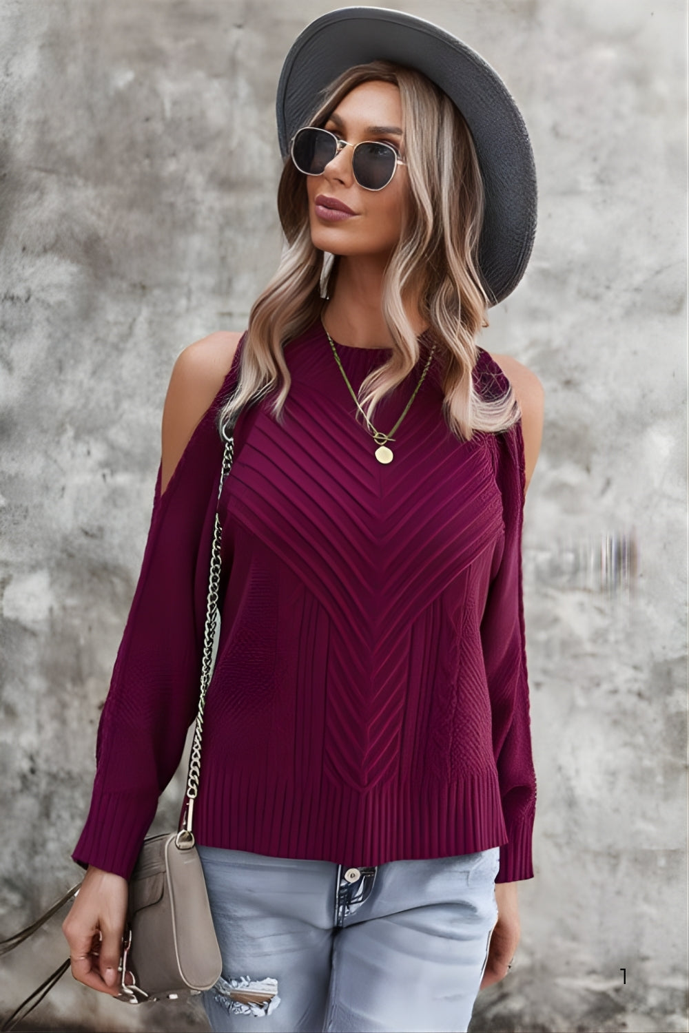 Woman wearing a purple sweater, gray hat, and sunglasses against a textured wall.