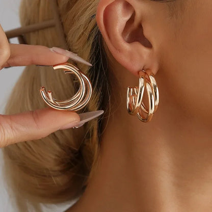 Gold hoop earrings being held up to a person's ear.