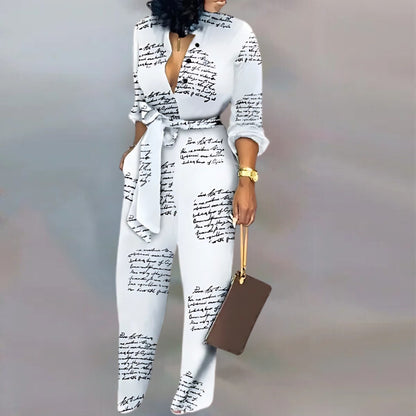  A person wearing a white jumpsuit featuring a black handwritten script design. The outfit has a plunging V-neckline, a cinched waist with a tied belt, and loose-fitting legs. Accessories include a gold wristwatch, a brown clutch with a gold strap, and open-toe high heels.