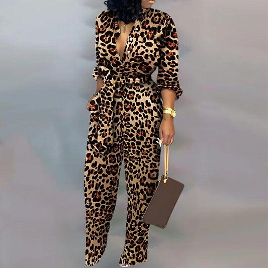  A fashionable leopard-pattern jumpsuit with rolled-up sleeves, a plunging neckline, and a belted waist. The outfit is paired with a brown rectangular bag, metallic heels, and a gold watch.