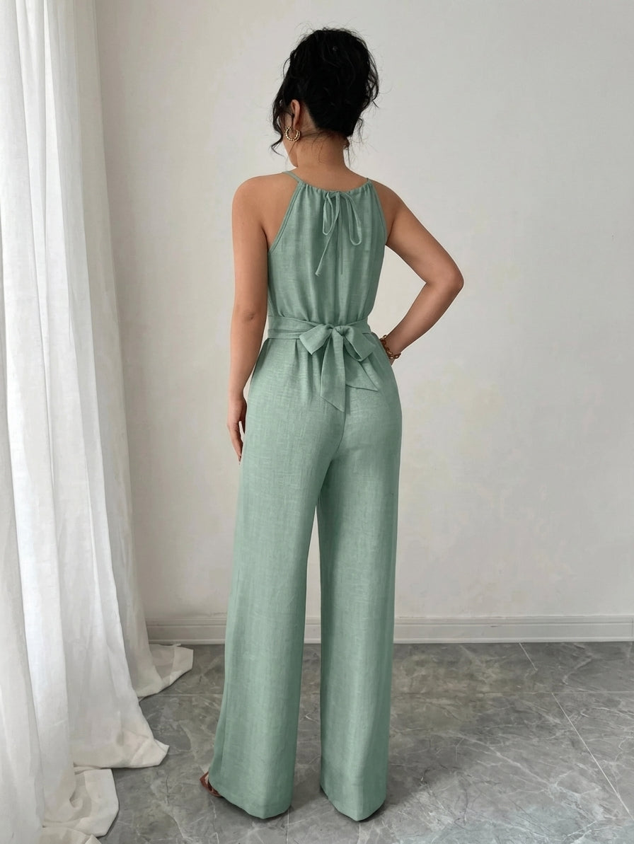 Woman wearing a green jumpsuit standing in a room with white curtains and gray floor.