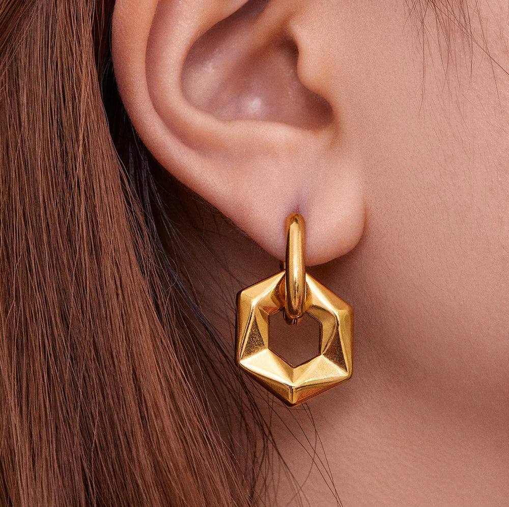 Gold hexagonal earring worn on an ear with a neutral background