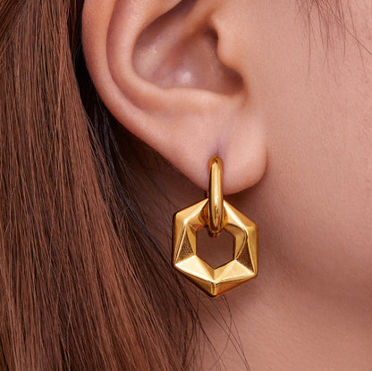Gold hexagonal earring worn on an ear with a neutral background