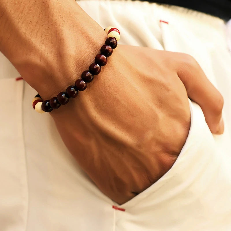 Close-up of a wrist wearing a dark beaded bracelet on a light background