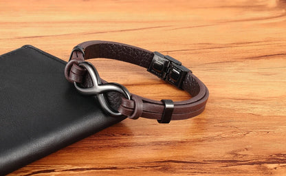 A dark brown leather bracelet with a unique interlocking infinity symbol clasp, resting on a black leather wallet over a wooden surface.