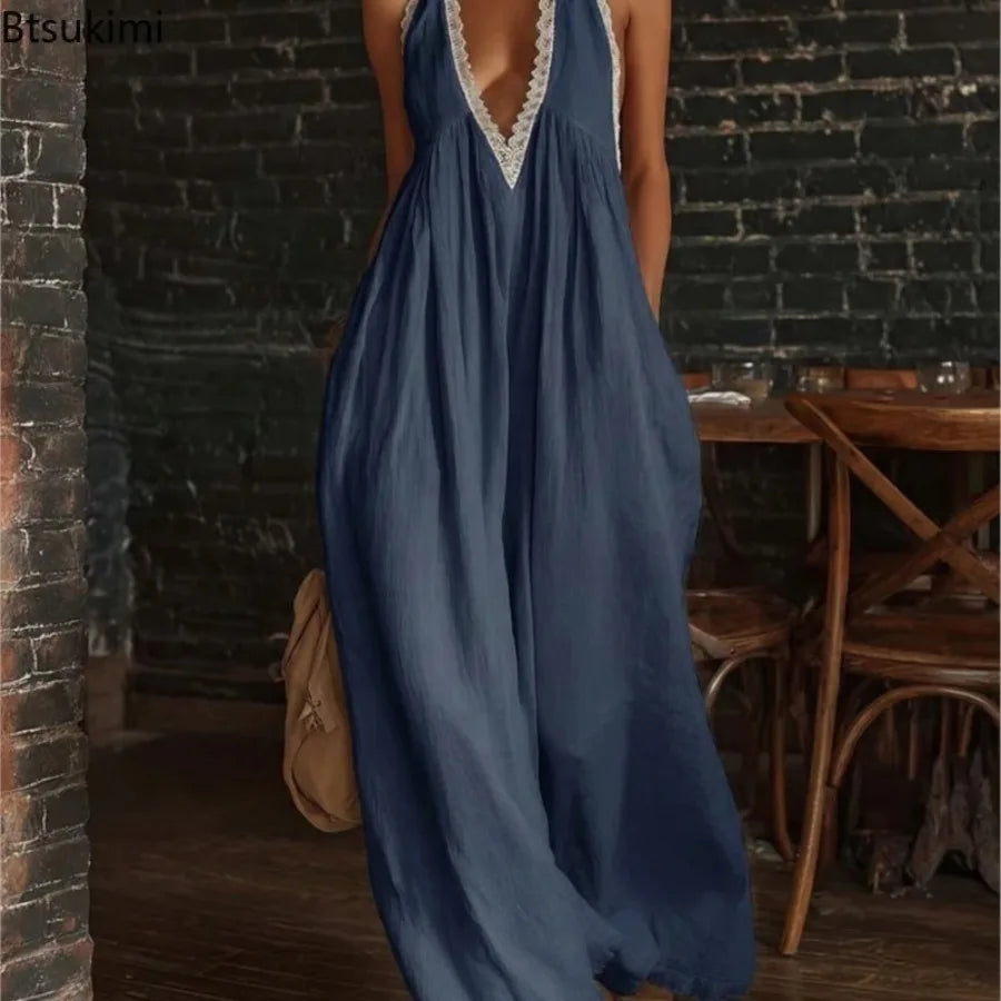 A woman wearing a loose, flowing maxi dress in muted blue with white lace trim at the neckline and armholes, standing in a rustic indoor setting with a dark brick wall and wooden furniture.