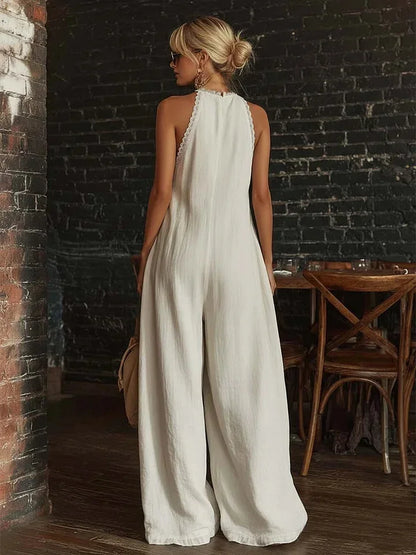 Woman in a white jumpsuit standing in a rustic indoor setting with brick walls and wooden furniture.