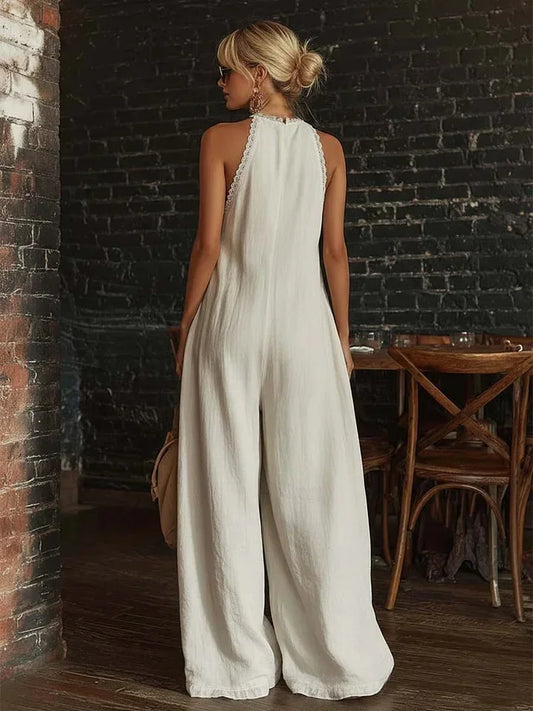 Woman in a white jumpsuit standing in a rustic indoor setting with brick walls and wooden furniture.