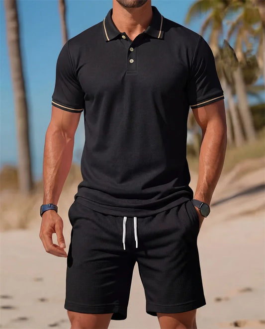 Man wearing a black polo shirt and shorts on a beach with palm trees in the background.