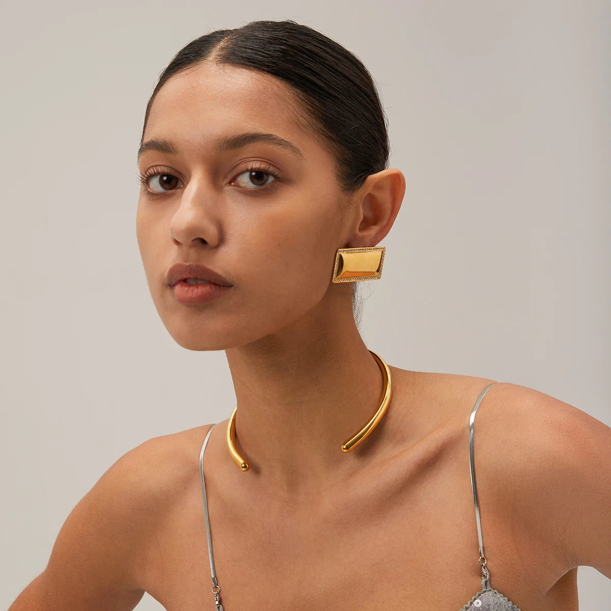 Woman wearing gold earrings and necklace against a neutral background