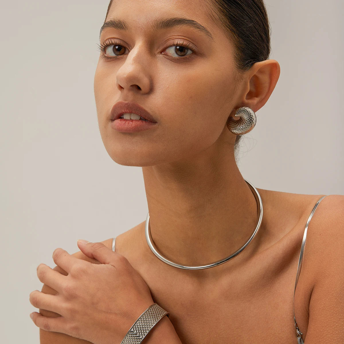 Woman wearing a silver necklace and earrings against a neutral background