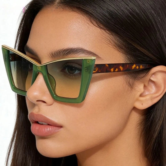A close-up of a woman wearing oversized square sunglasses with a green front frame, gold metal trim, gradient amber lenses, and tortoiseshell-patterned temples. The pink text 'DOHOHO' appears in the top left corner.