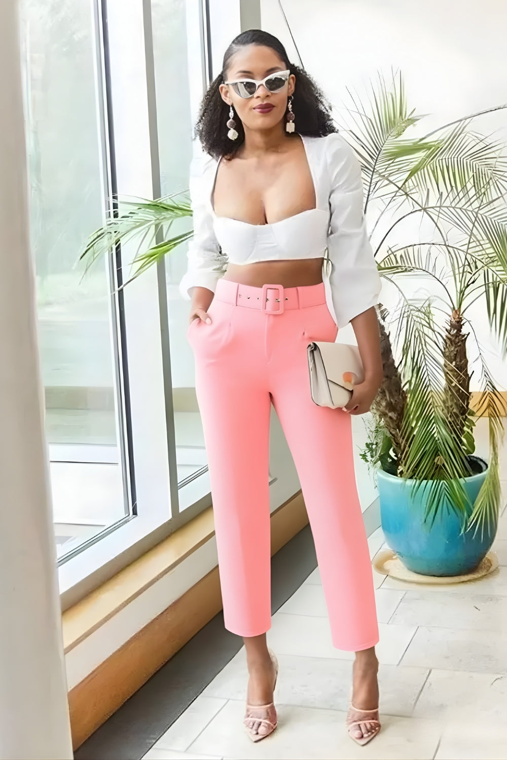Woman in white top and pink pants standing indoors with plants in the background
