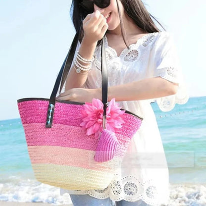 Woman holding a colorful straw bag with a pink flower on a beach.