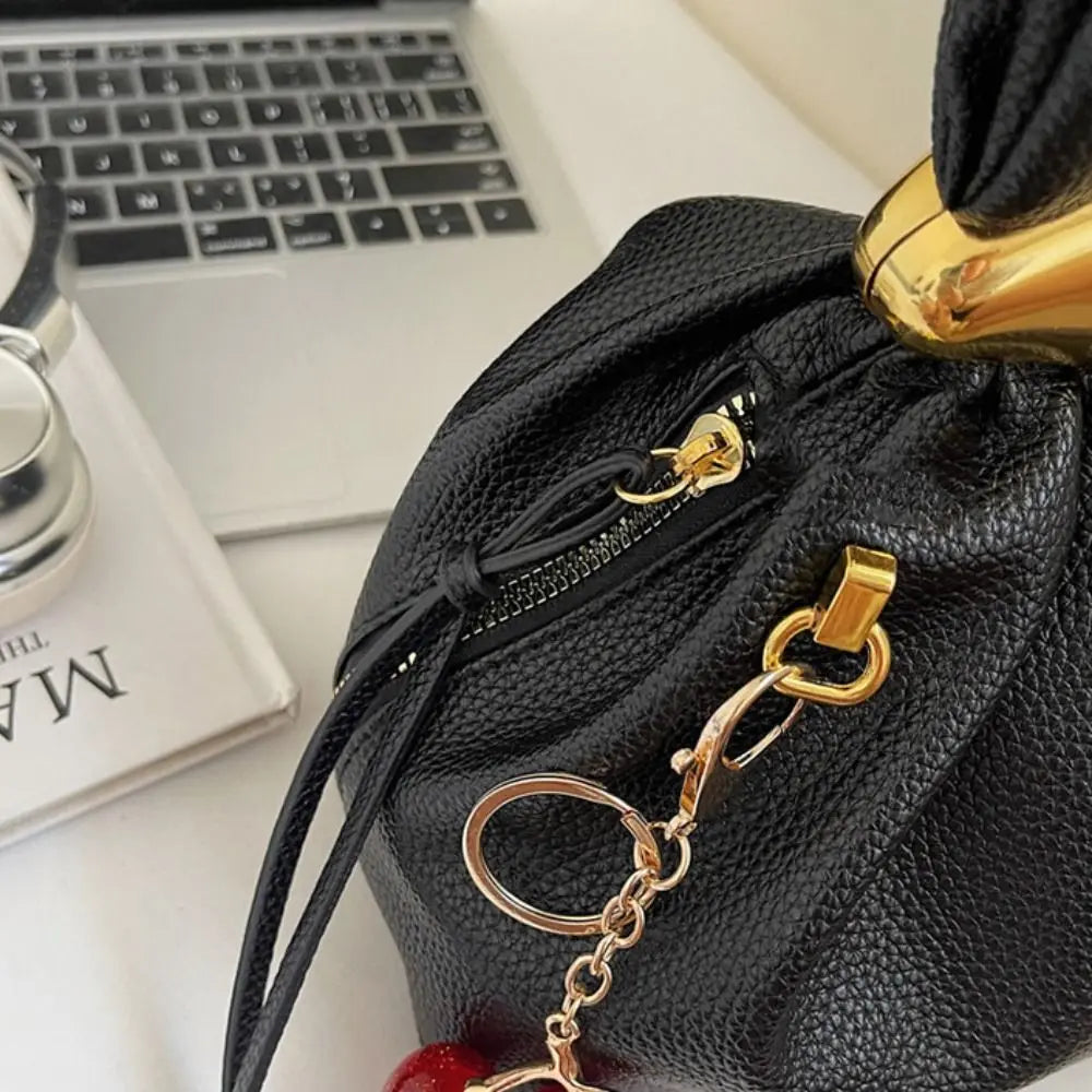 Black drawstring bag with gold keychain and ring on a desk with a laptop and book.