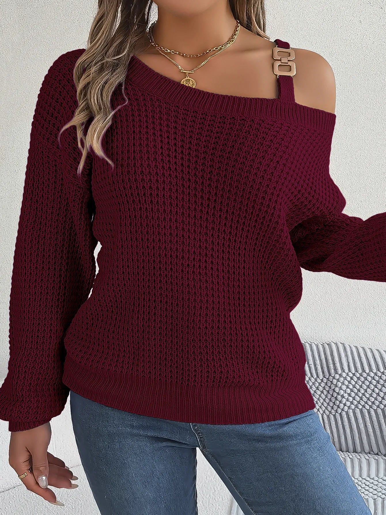 Person wearing a burgundy off-shoulder sweater with blue jeans on a light background