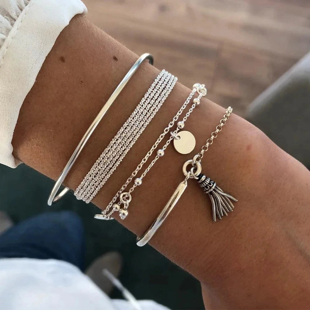 Close-up of a wrist wearing multiple silver and gold bracelets with charms.