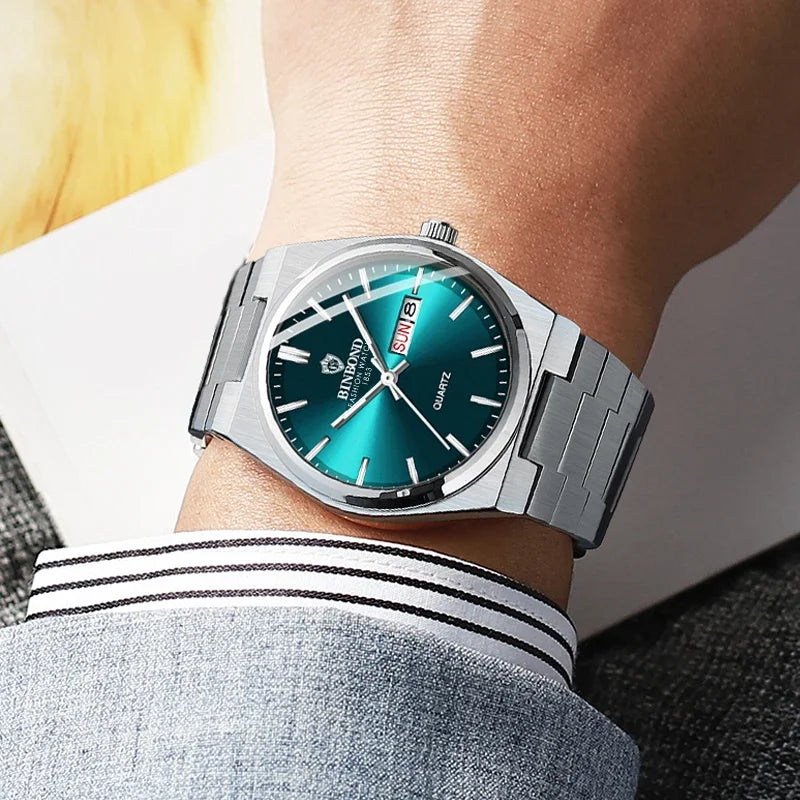 Silver watch with a green face on a person's wrist, wearing a gray shirt with white stripes.