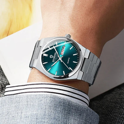 Silver watch with a green face on a person's wrist, wearing a gray shirt with white stripes.