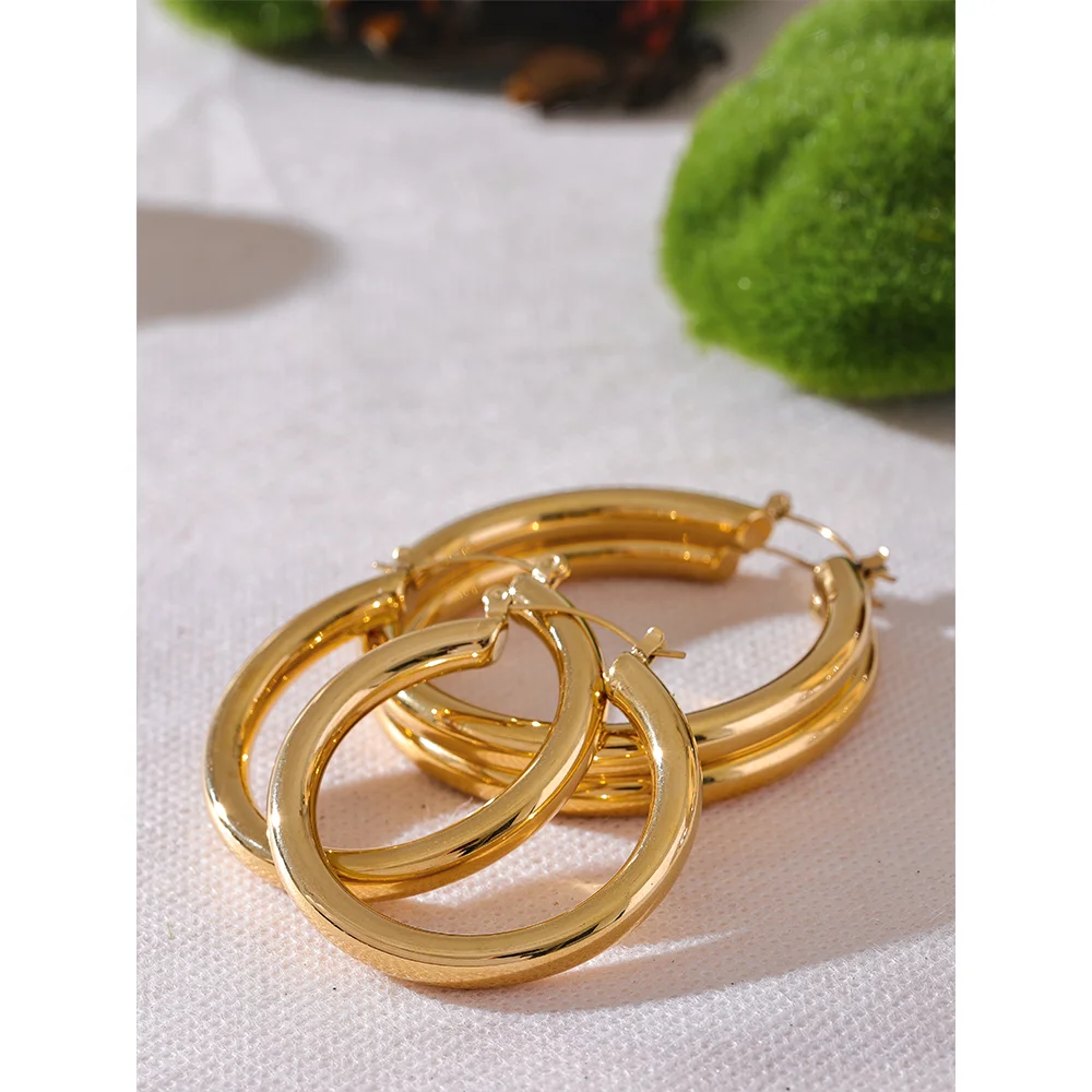 Gold hoop earrings on a white fabric background with green decorative elements.
