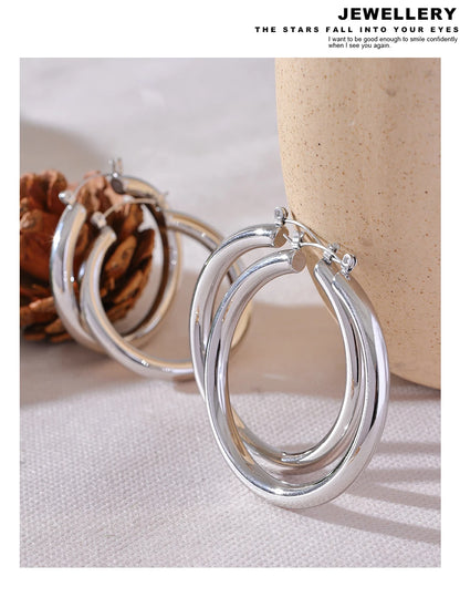 Silver hoop earrings on a textured surface with a neutral background