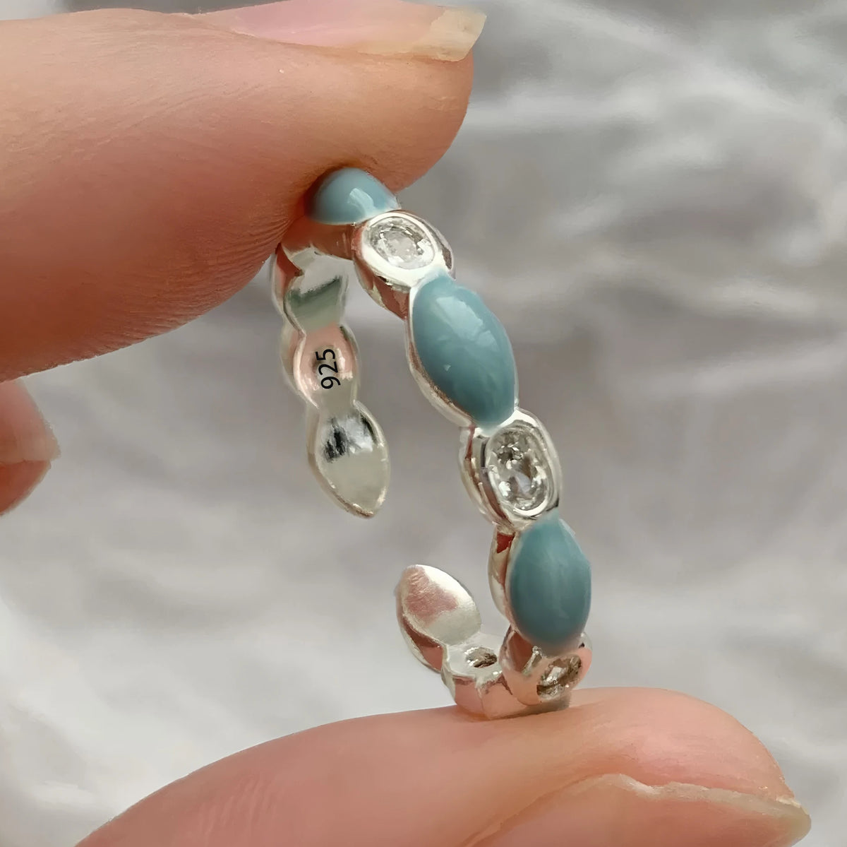 Silver ring with blue beads held between fingers against a neutral background
