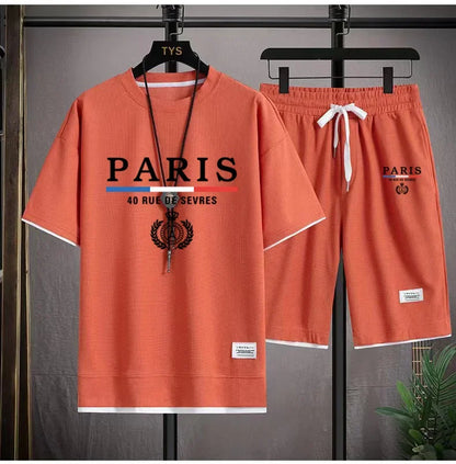 Orange 'Paris' themed t-shirt and shorts set on hangers against a gray background.