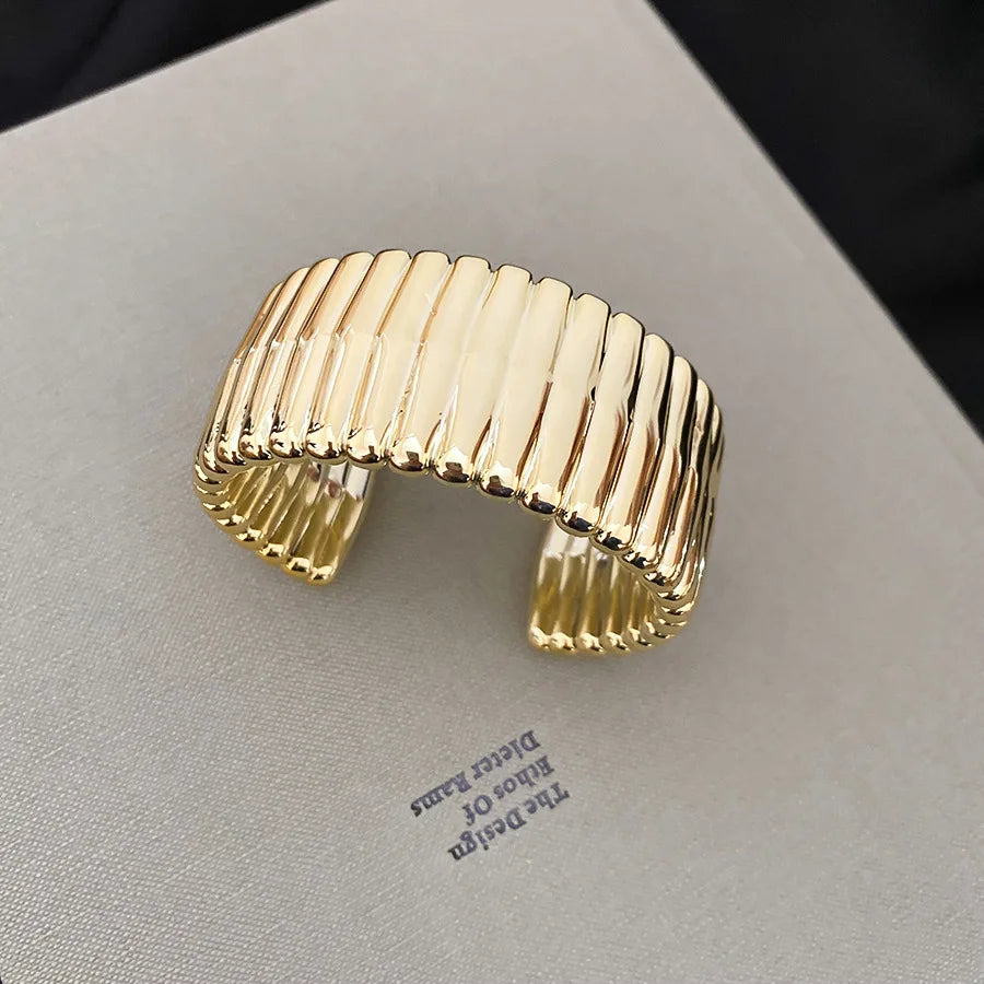 Gold ribbed cuff bracelet on a light gray surface