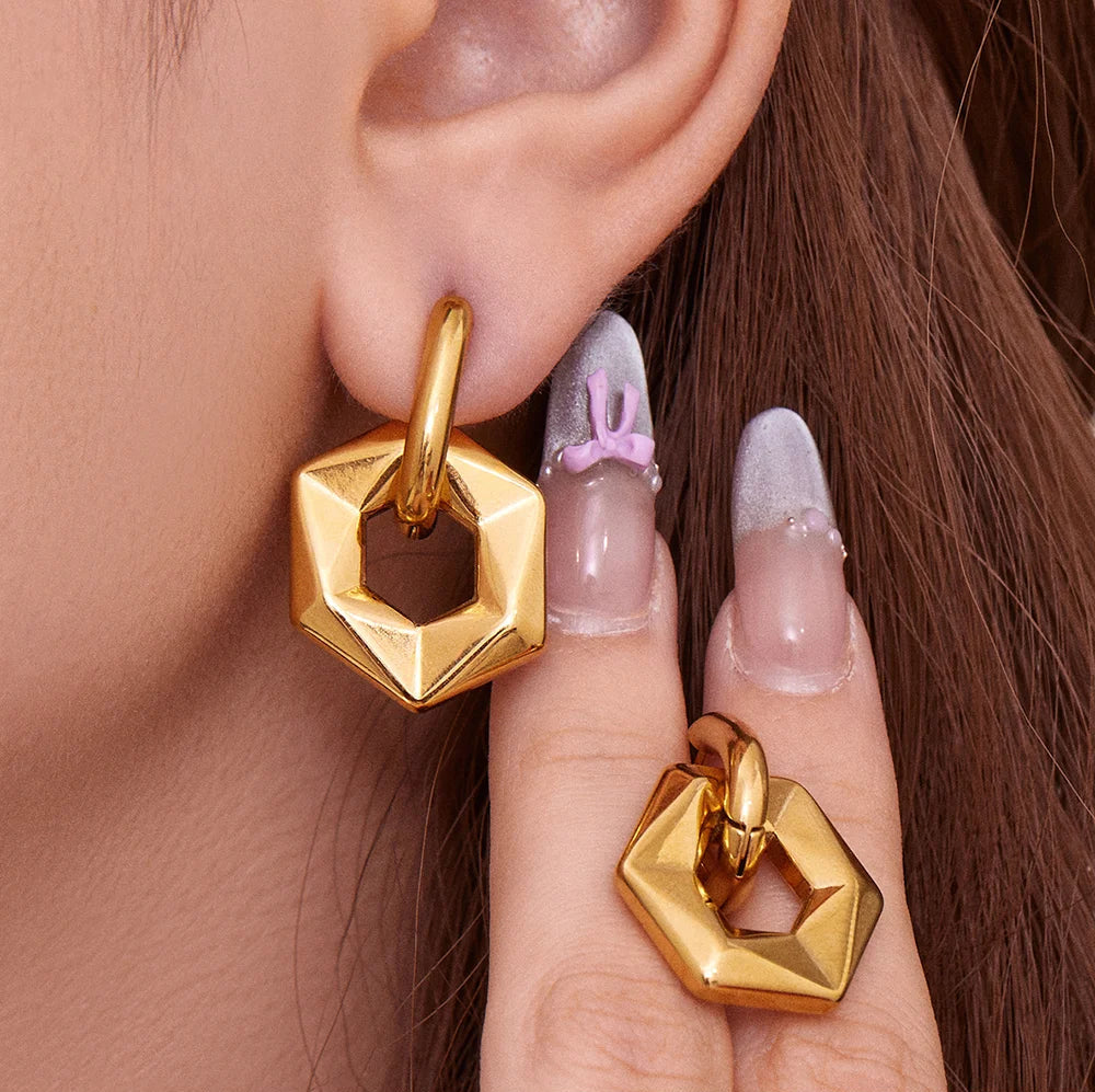 Gold geometric earrings worn by a person with a neutral background