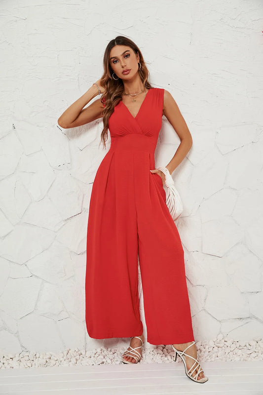 A woman in a red sleeveless V-neck jumpsuit with wide-leg pants, paired with heels and a handbag.