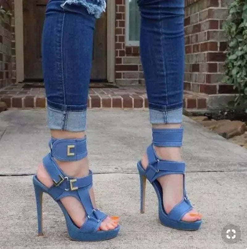 Blue high-heeled sandals worn with rolled-up jeans on a concrete surface.